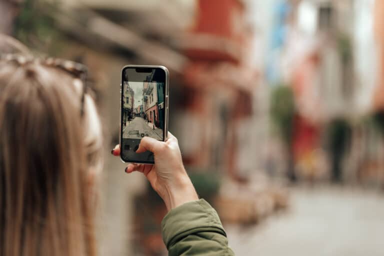 Woman tourist taking photo with phone in the street back view